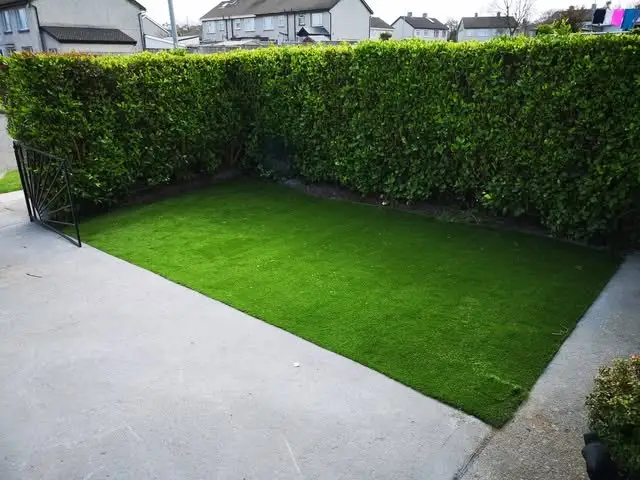 After: green artificial grass covering the yard up to the hedge