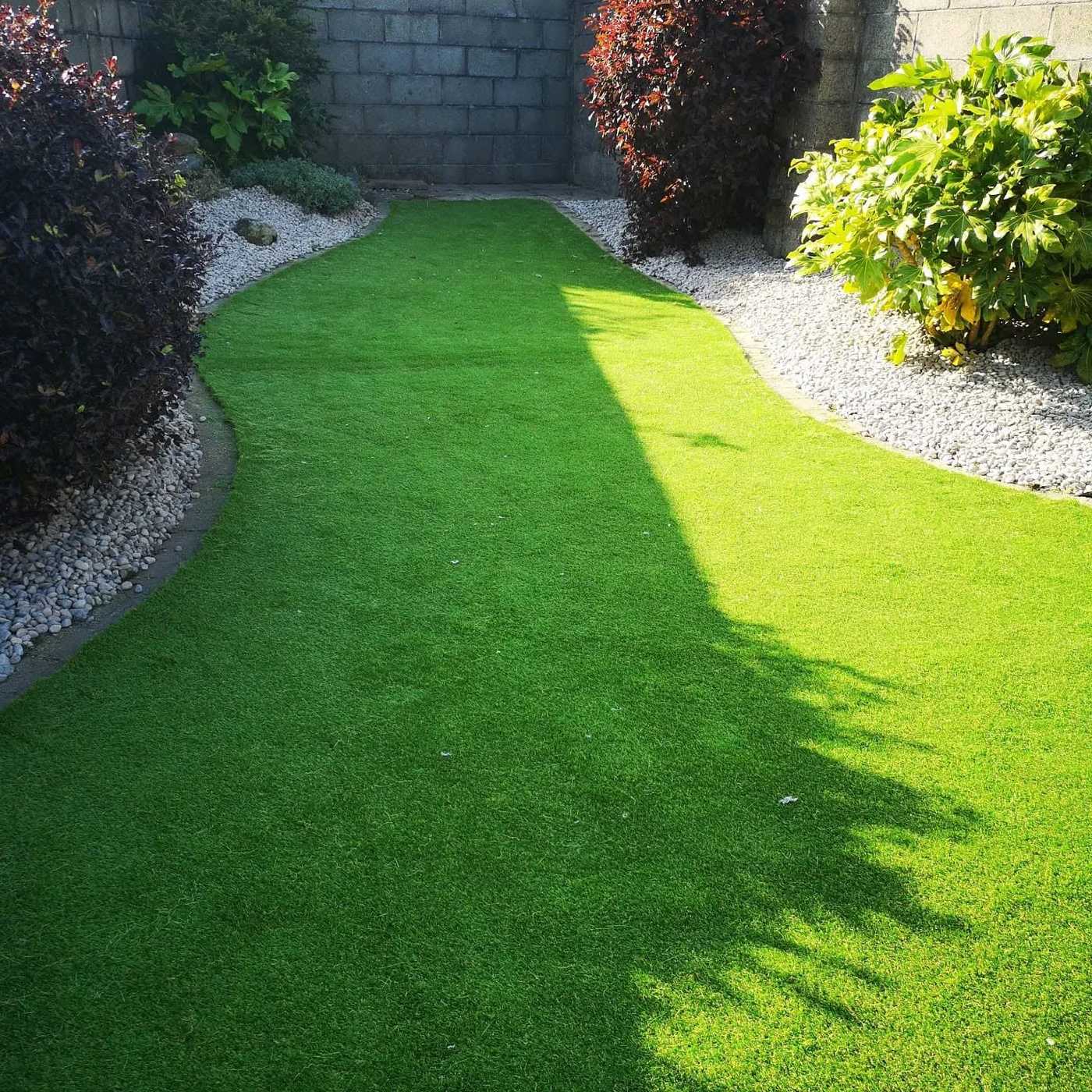 Curved artificial lawn edged with white pebbles and shrubs