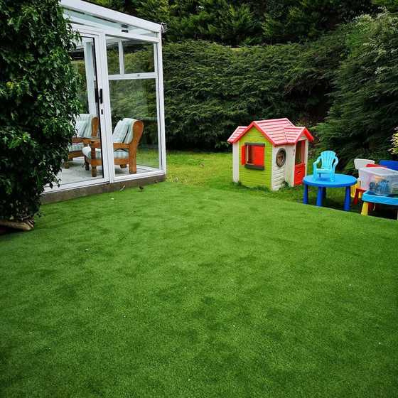 Artificial lawn beside a conservatory with a children’s playhouse and toys
