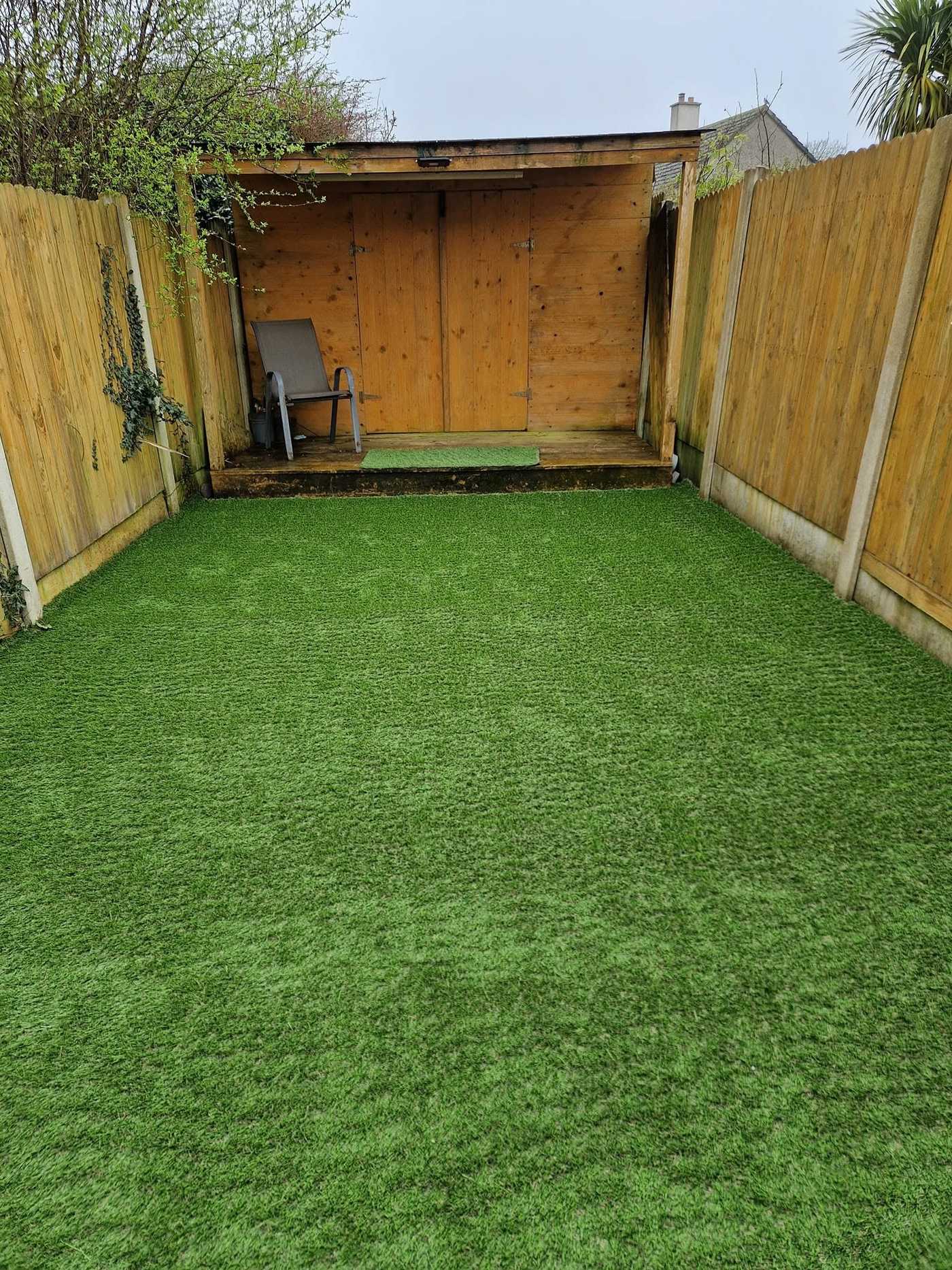 Fenced back garden with artificial grass leading to a timber summer house