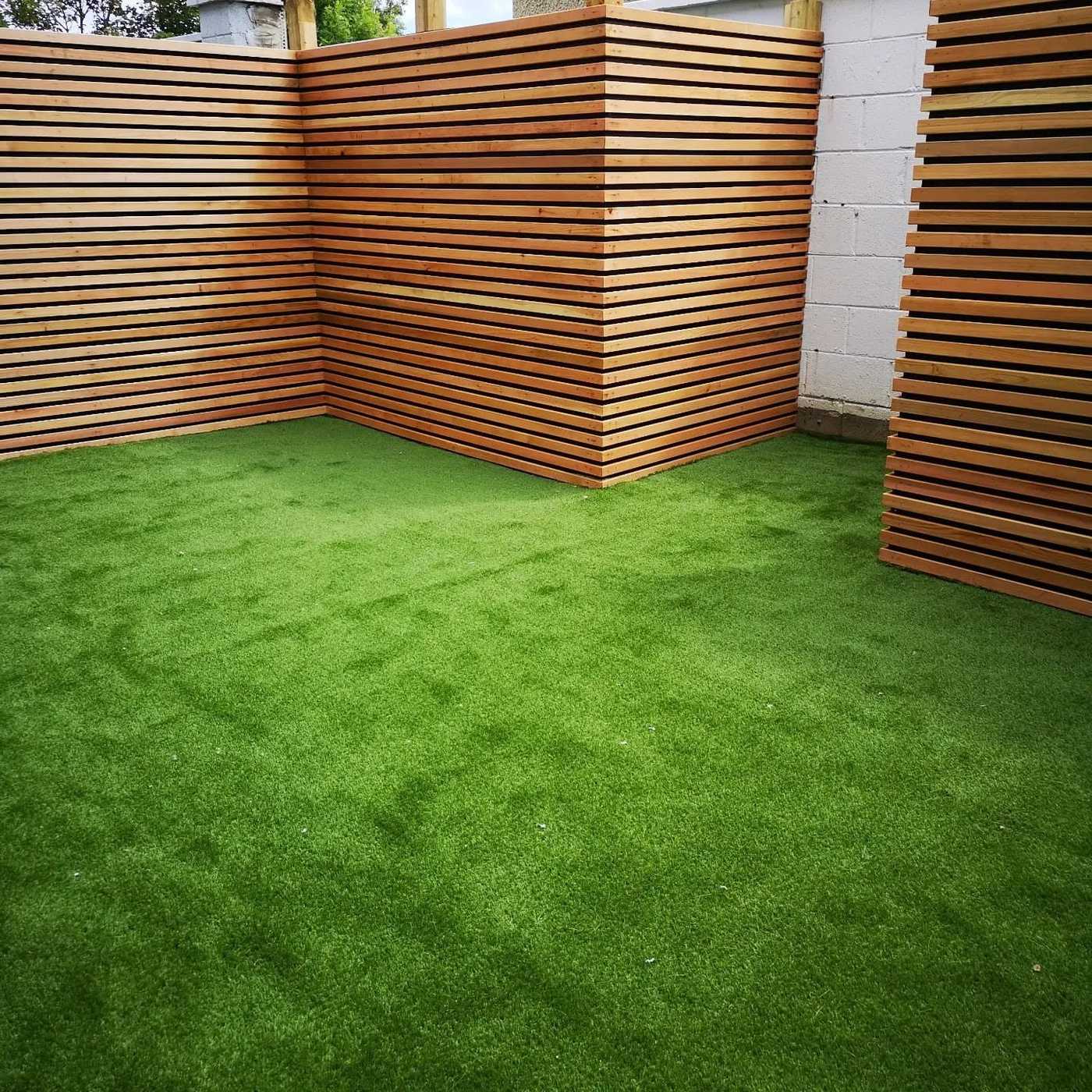 Artificial lawn meeting horizontal slatted timber fence panels