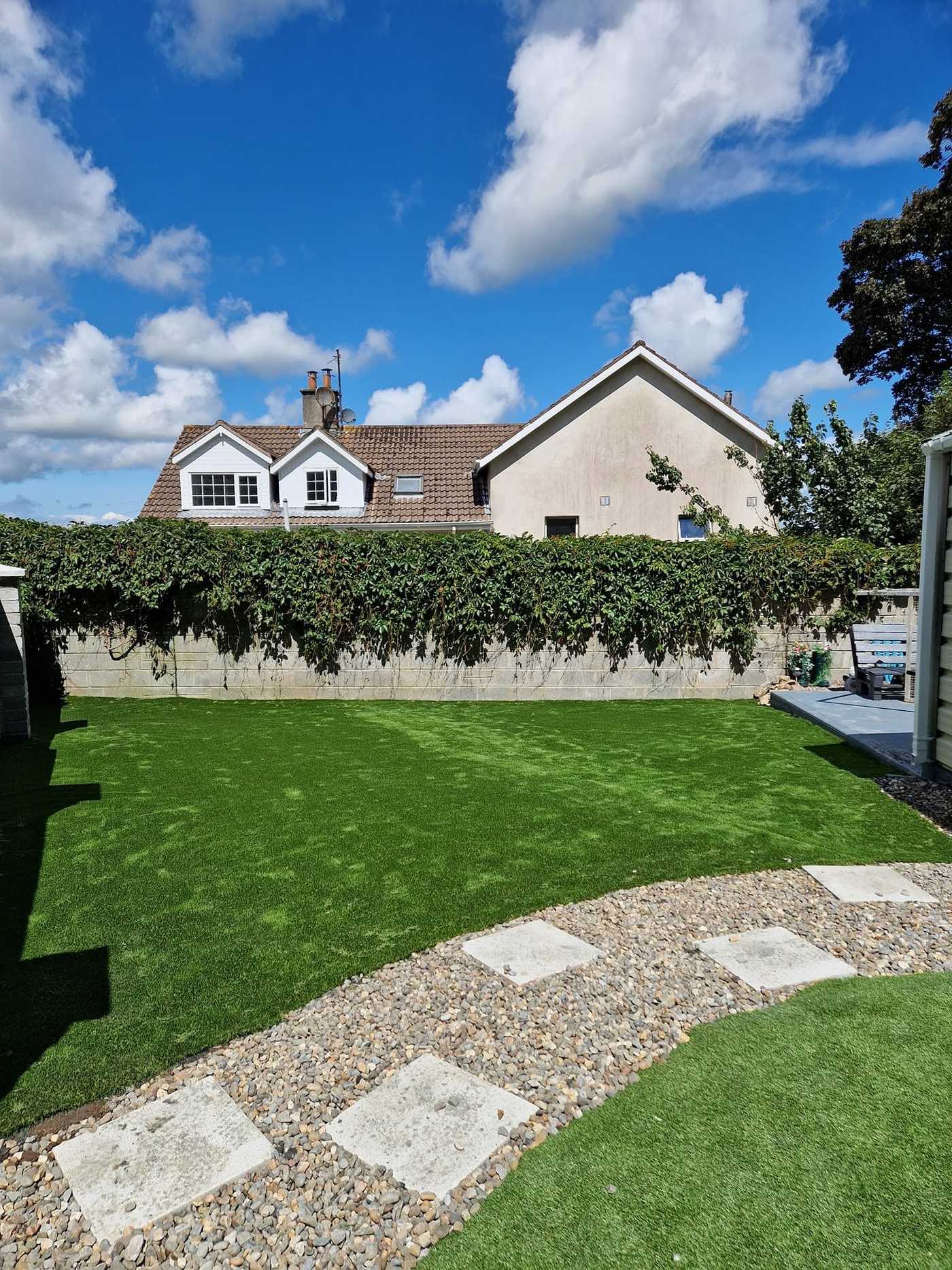 Artificial lawn with stepping stones and a gravel path in front of a house