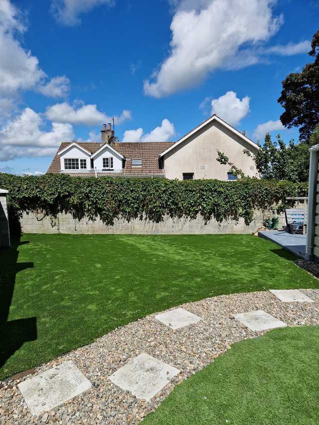 Artificial lawn with stepping stones and a gravel path in front of a house