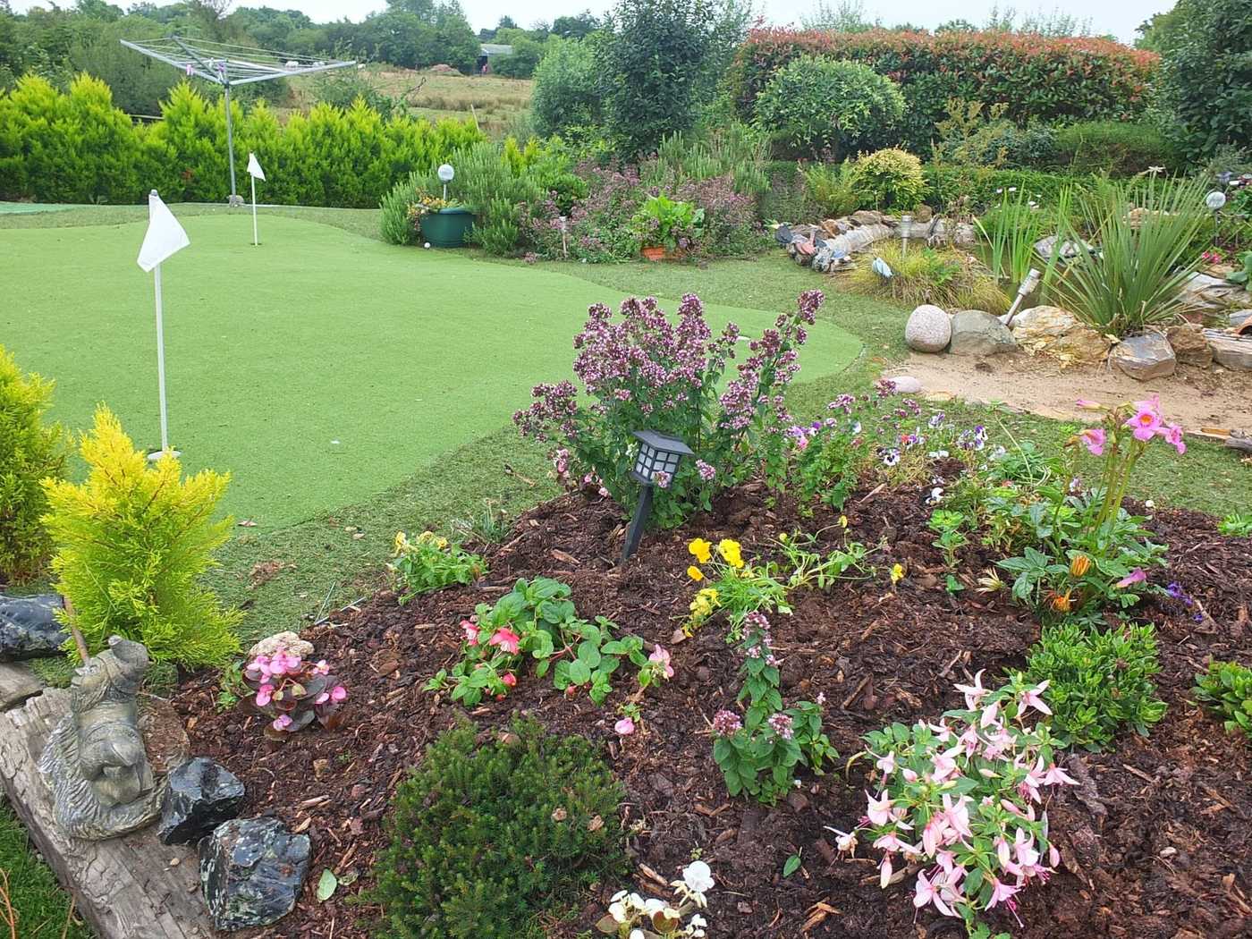 Garden putting green with a flag, surrounded by flower beds and a rockery