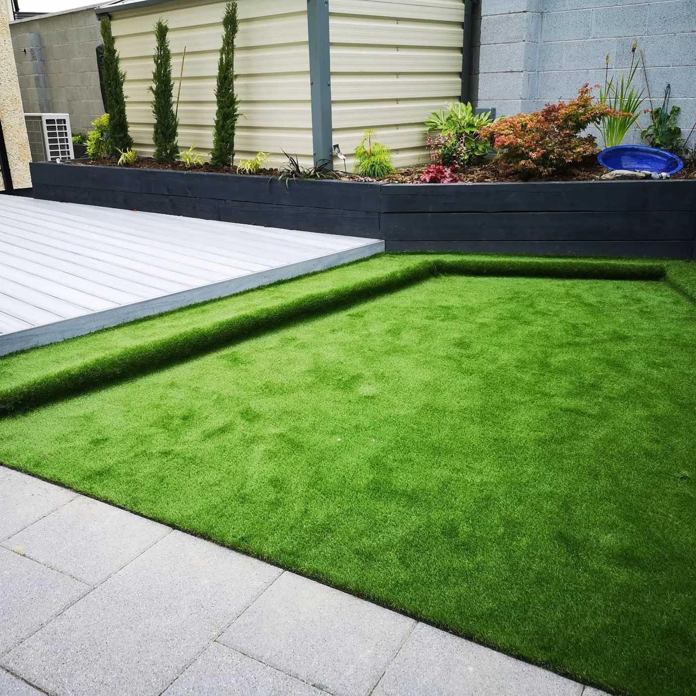 Artificial lawn between grey composite decking, paving and raised planters