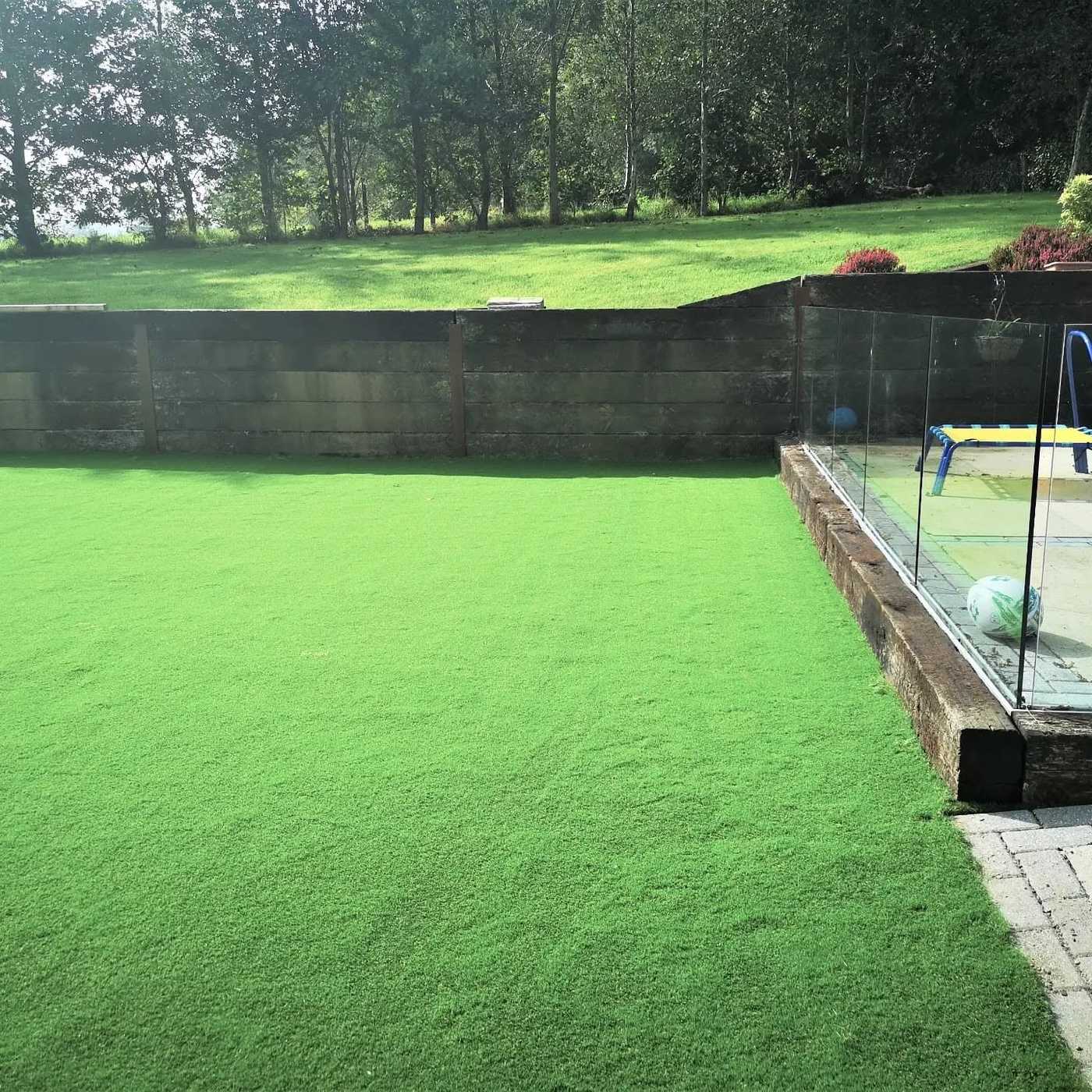 Artificial lawn running up to a glass balustrade and timber sleeper wall