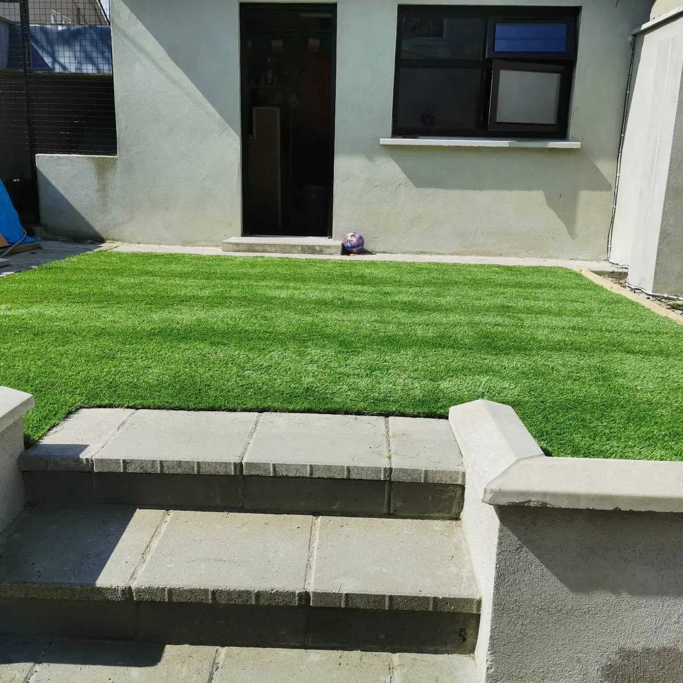 Artificial lawn at the top of concrete patio steps behind a house
