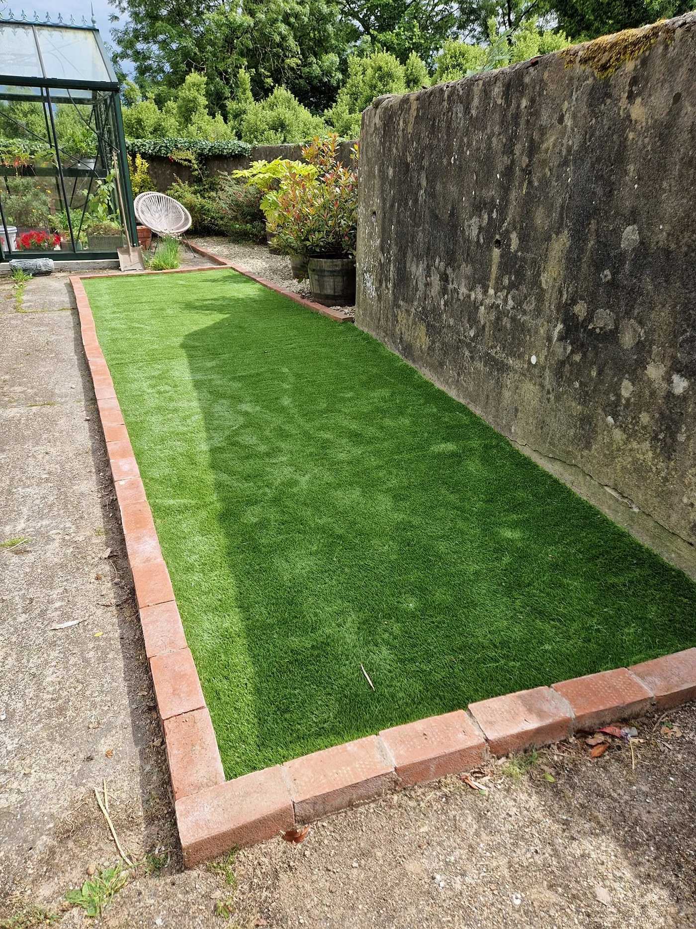 Long narrow strip of artificial grass edged with red brick beside a stone wall