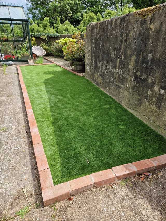 Long narrow strip of artificial grass edged with red brick beside a stone wall