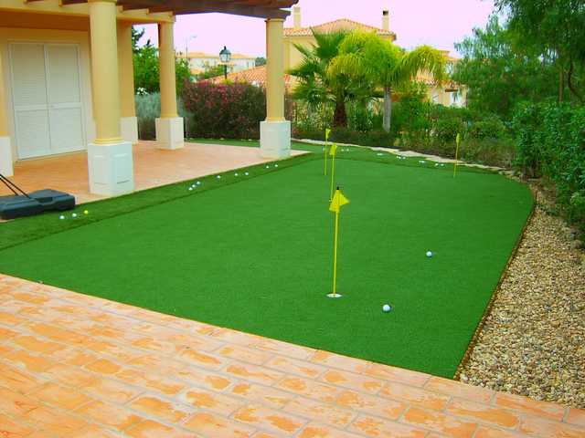 Putting green with yellow flags and golf balls beside a terracotta patio