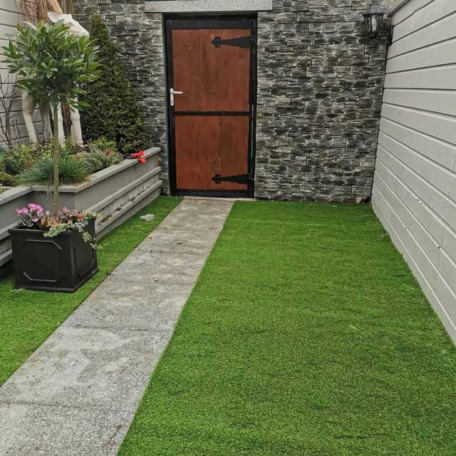 Narrow courtyard garden with a stone wall, timber door, paved path and artificial lawn